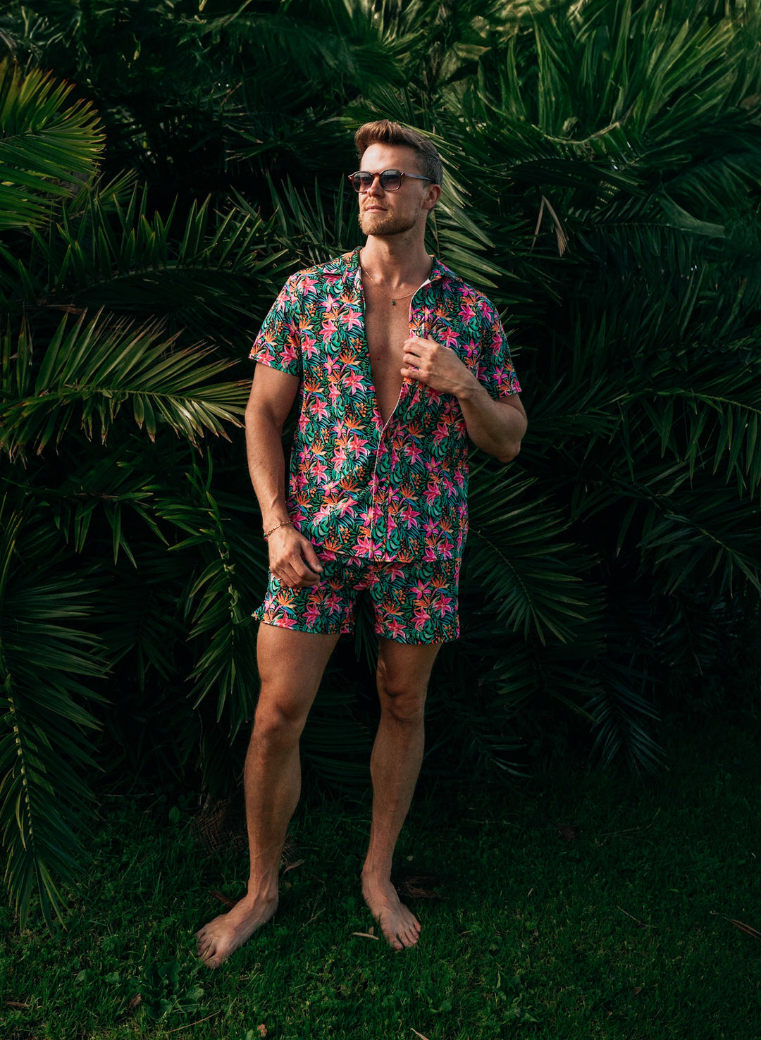 Salty Mermaid men’s tropical floral swimwear set, button-down shirt and matching trunks, modeled in a relaxed full-body shot against palm leaves