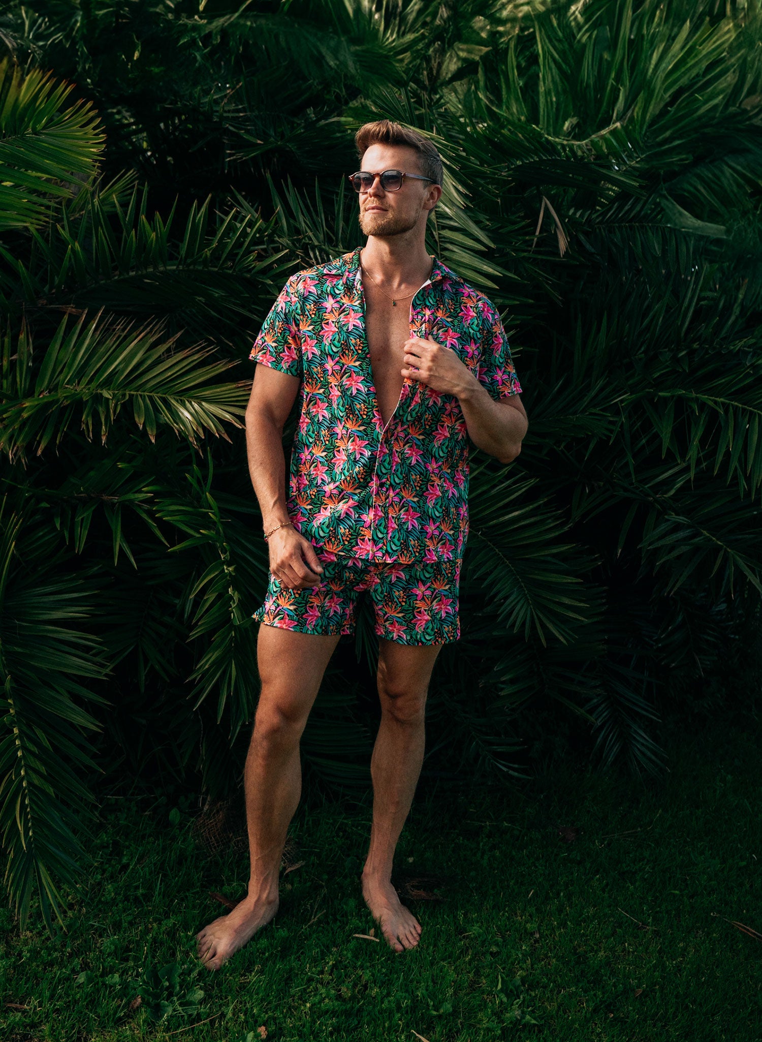 Salty Mermaid men’s tropical floral swimwear set, button-down shirt and matching trunks, modeled in a relaxed full-body shot against palm leaves