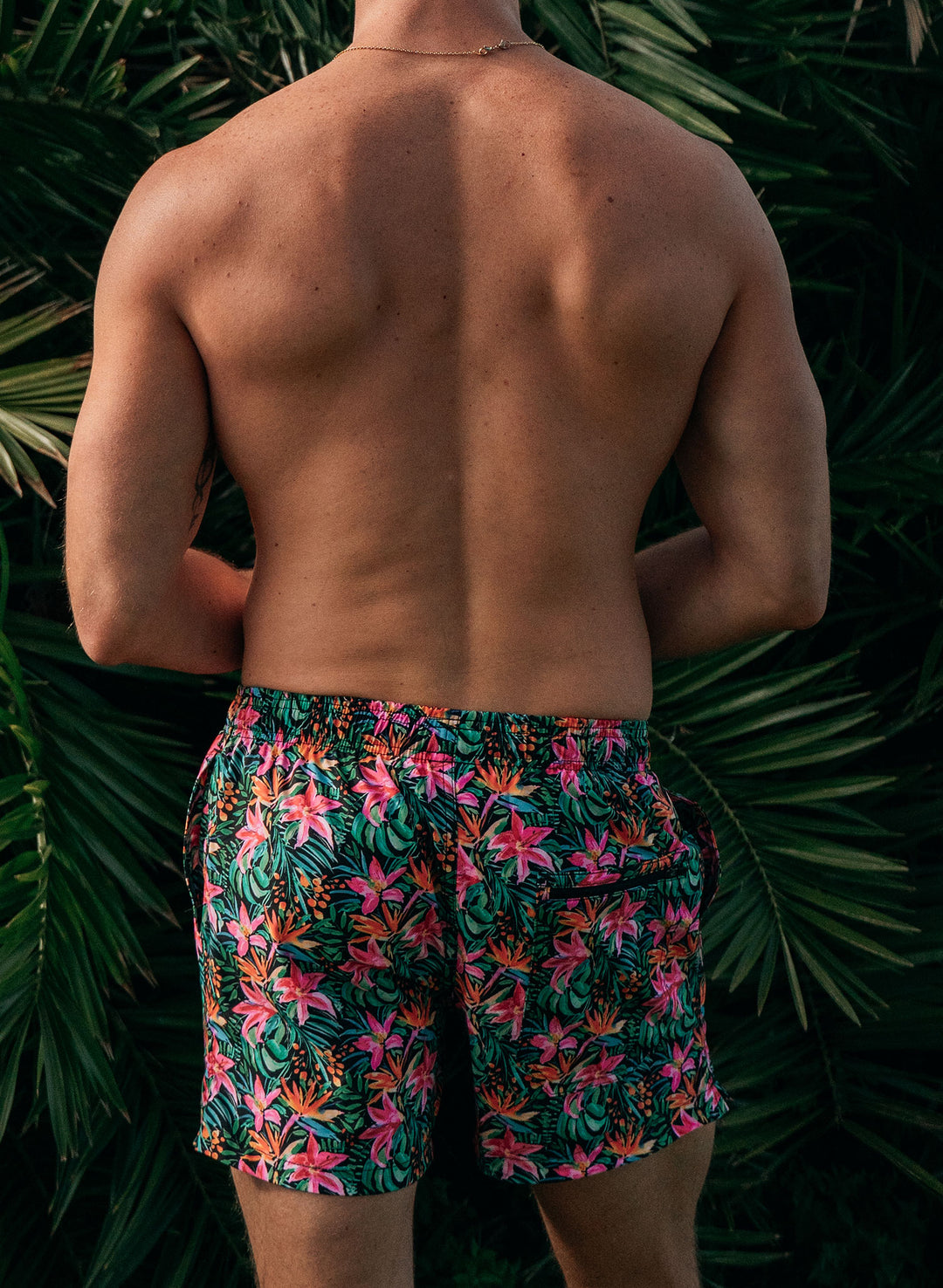 Man wearing Salty Mermaid Island Bloom tropical floral swim trunks with bold pink, green, and orange floral print, 4–5" inseam.