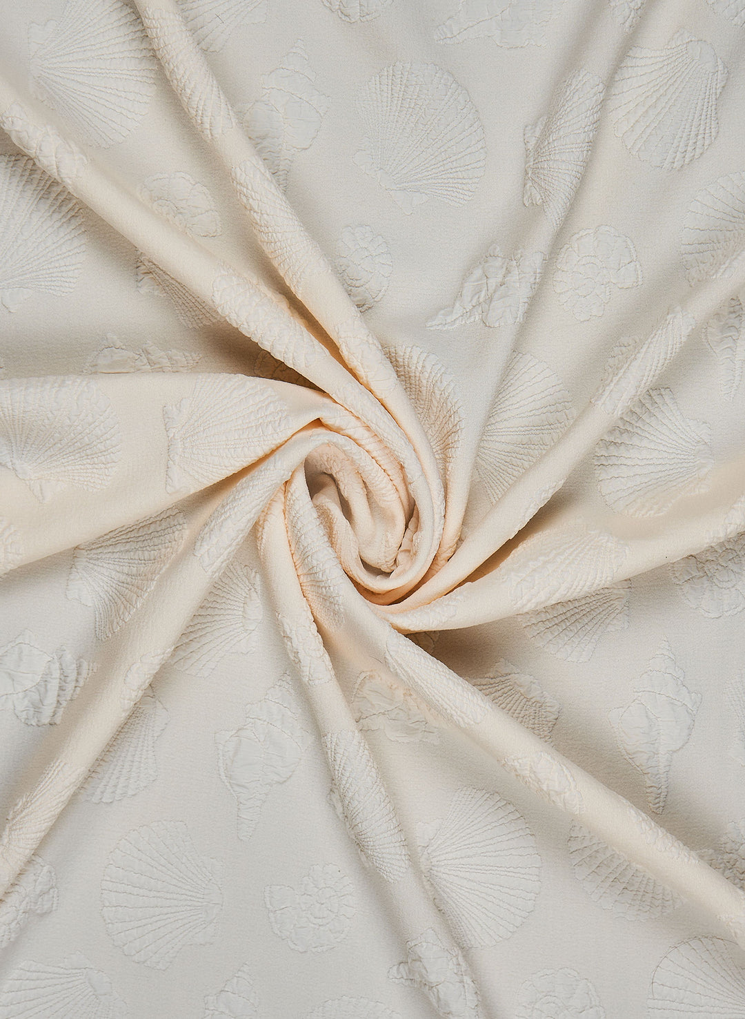 Close-up of ivory shoreline embossed fabric swatch featuring raised seashell patterns and soft textured detailing, twisted in a swirl to showcase drape and design.