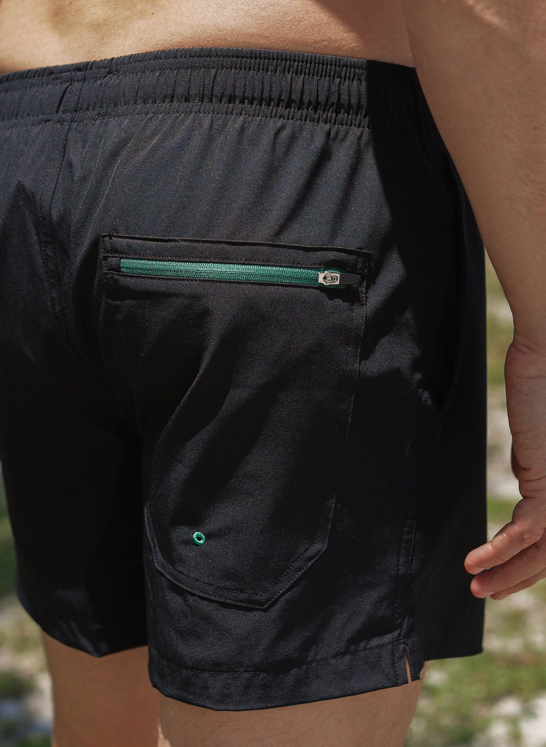 Black swim trunks with zippered back pocket detail on men’s solid black swim trunks—Salty Mermaid