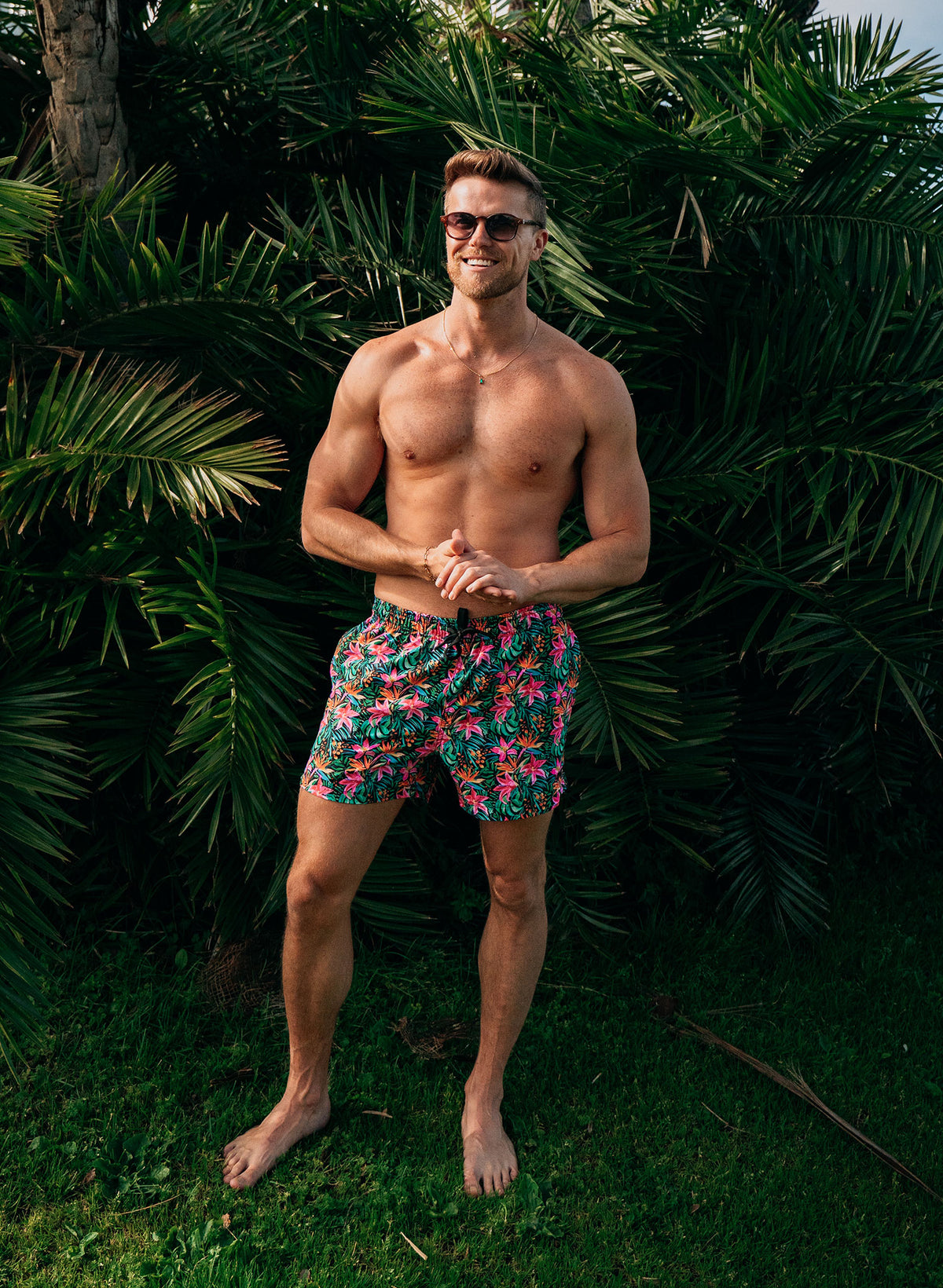 Men’s Island Bloom swim trunks featuring vibrant tropical floral print, front and back views with braided drawstring waistband, zipper pocket, and mesh liner with hidden pocket. Styled with matching shirt for coordinated beachwear. Perfect for couples matching swimwear in the Island Bloom collection by Salty Mermaid. Men’s Island Bloom button-up shirt in tropical floral print, shown in front and back views. Styled open over matching swim trunks for a coordinated resort outfit. Features lightweight fabric,