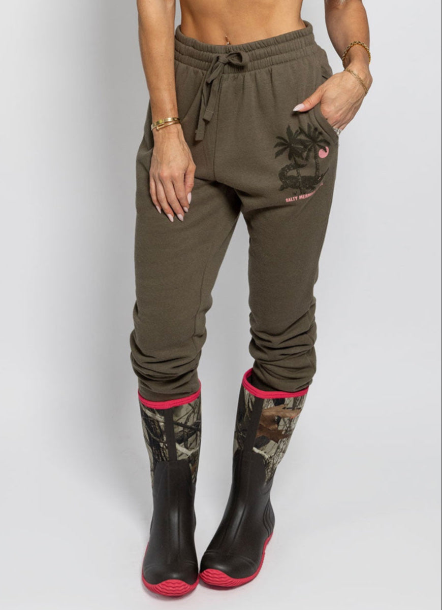 model wearing dark greenish brown sweat joggers with aligator print and camo duck boots. salty mermaid