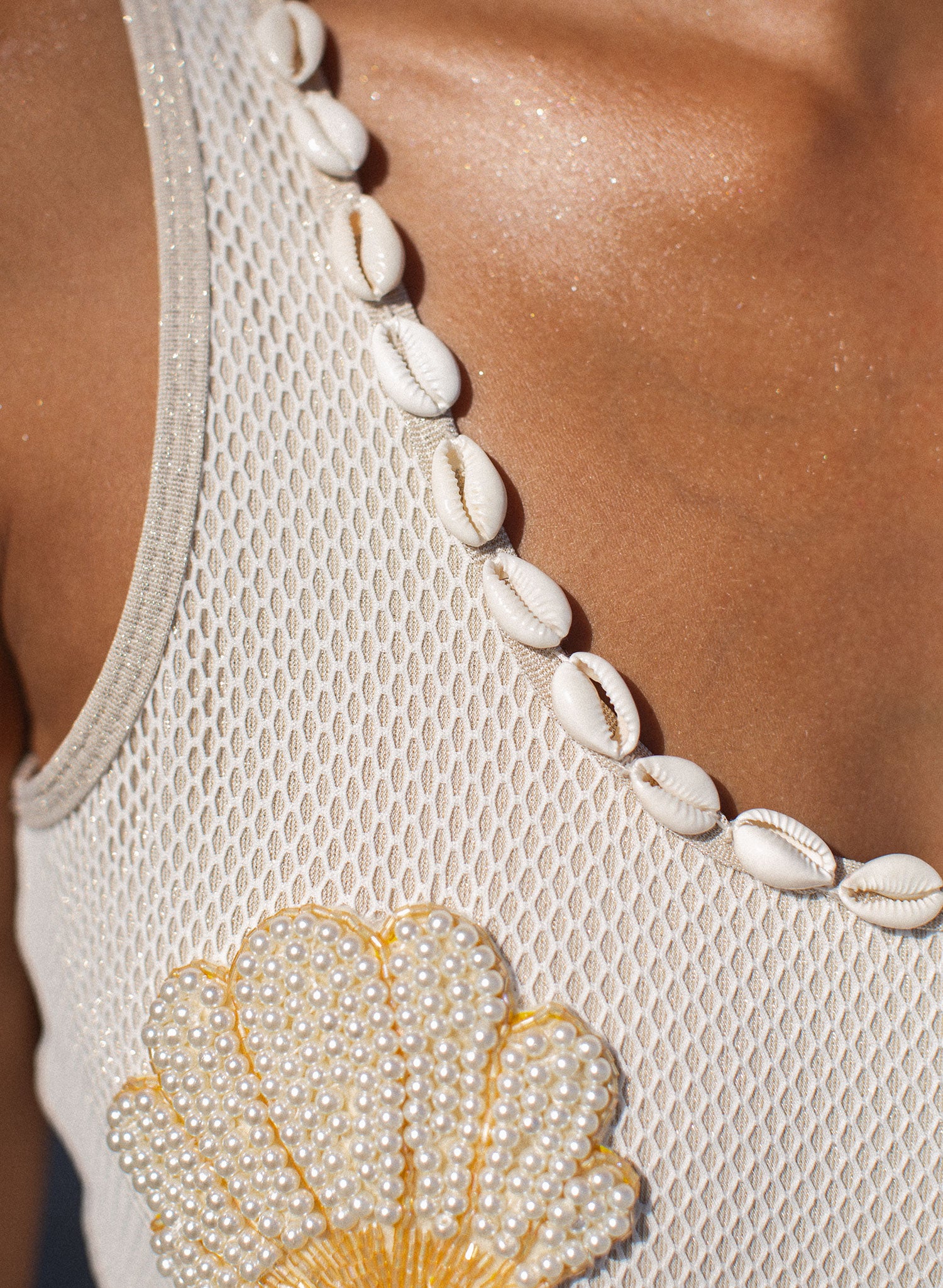 Close-up women’s one-piece swimsuit with seashell neckline trim and pearl shell applique, mesh texture