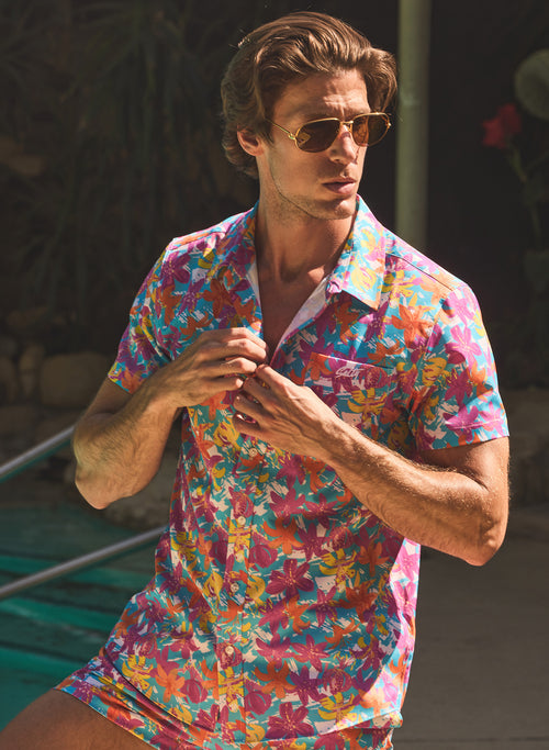 Man wearing a 70s inspired hawaiian floral matching swim trunks and shirt set by salty mermaid hot tropic collection