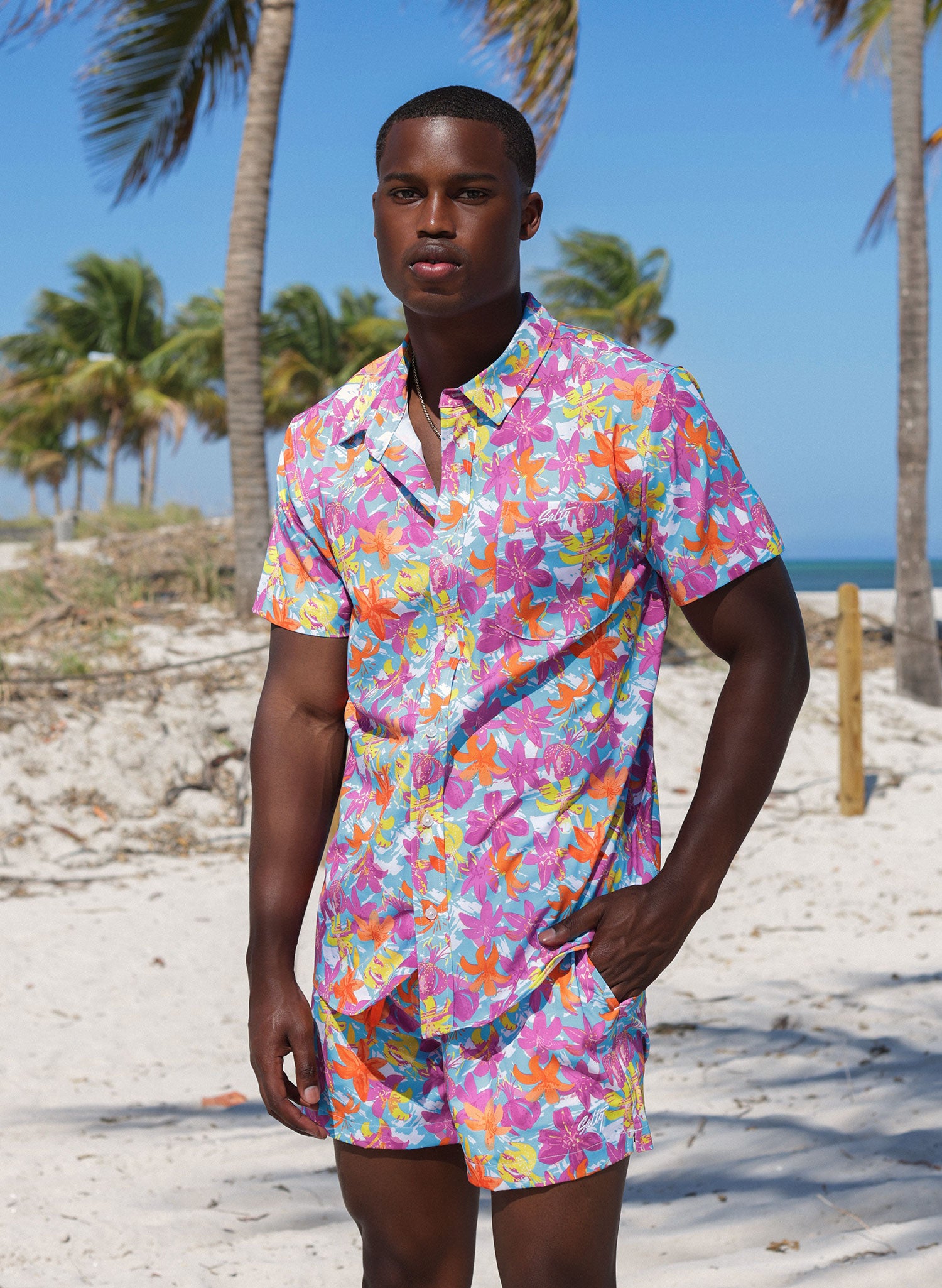 Salty Mermaid men’s button-down Hawaiian shirt in Hot Tropic, vintage tropical floral print with pink, orange, and blue flowers on the beach