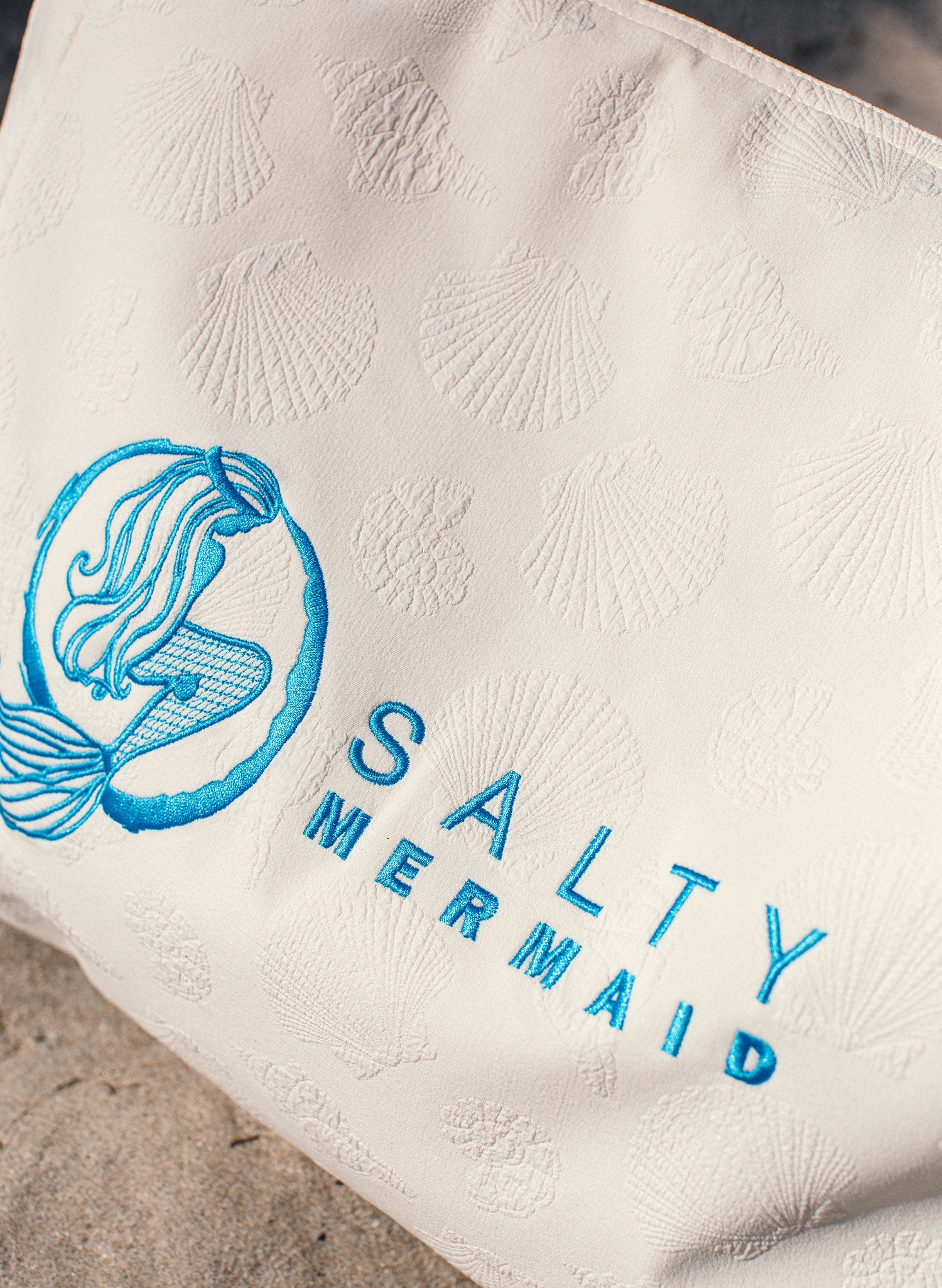 Ivory beach tote close-up with seashell texture and blue embroidered Salty Mermaid logo