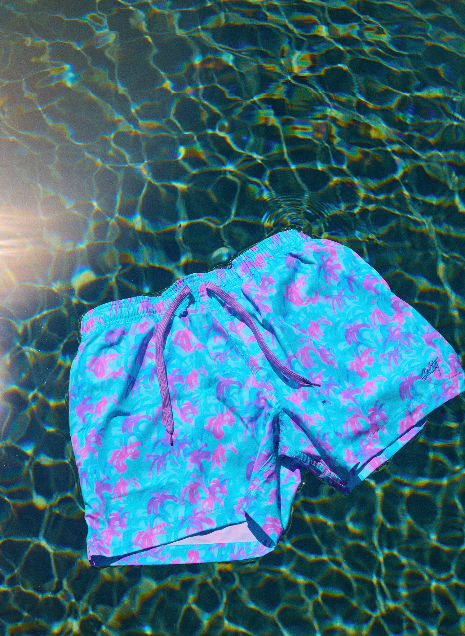 men's Palm tree Floral-pattern swim shorts floating in a pool in the sun by salty mermaid swimwear