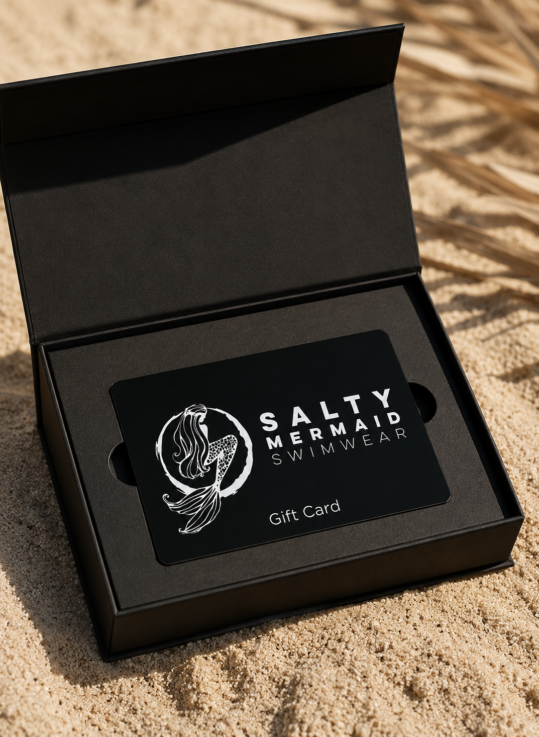 Salty Mermaid Swimwear gift card in a black box on sand
