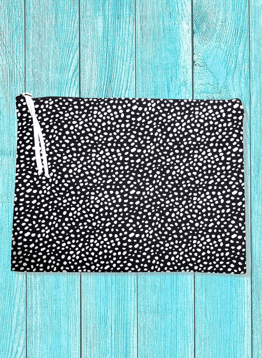 A black and pink polka dot printed bikini bag with a zipper top closure, displayed on a wooden blue background.
