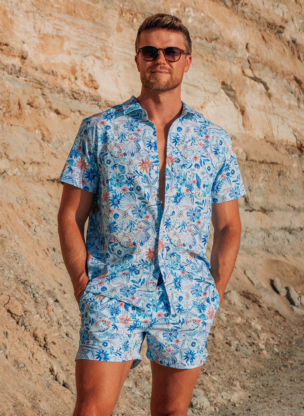 Salty Mermaid men’s resort set featuring button-down shirt and swim shorts with tropical floral and seashell motif in a hand-drawn style, Nautical Garden collection.
