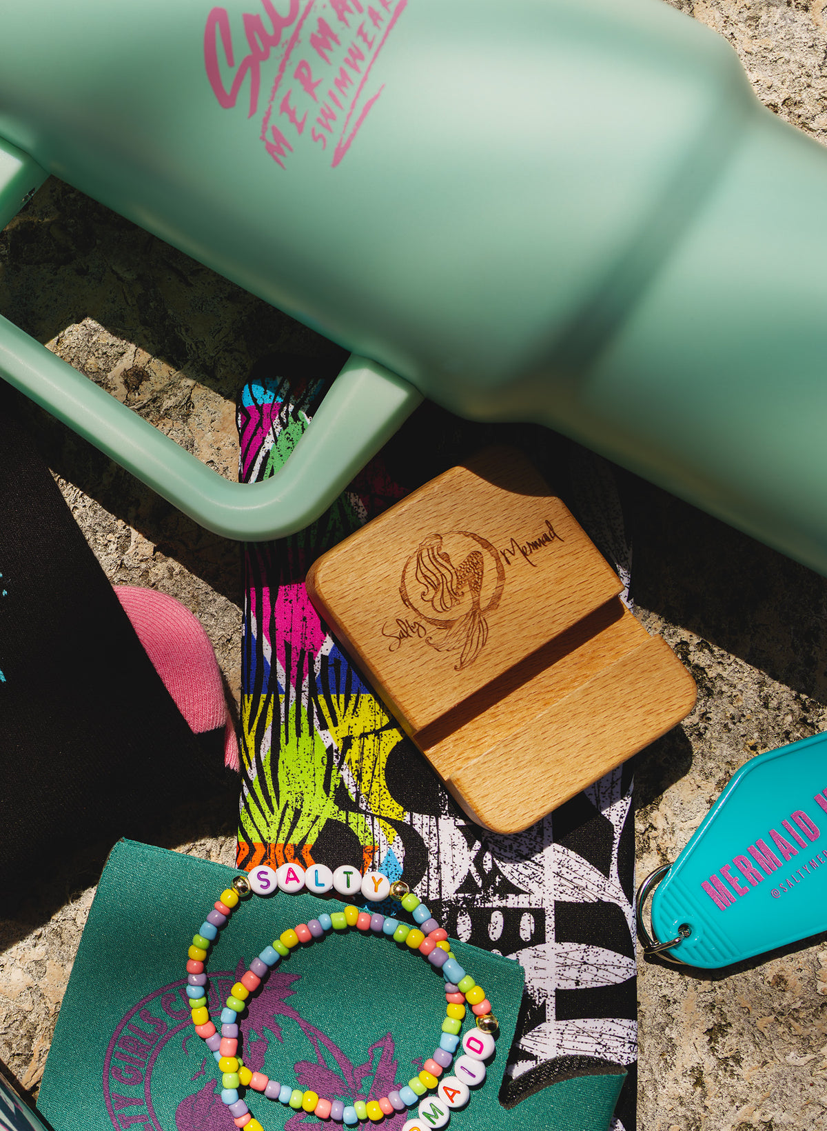 Salty Mermaid Mystery Box preview with a mint handled tumbler, wooden phone stand, colorful friendship bracelets and turquoise keychain.