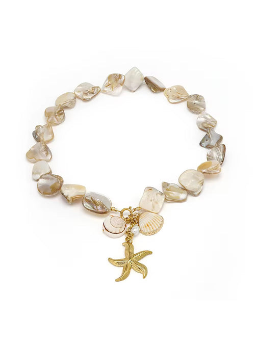 A sahira beaded shell charm bracelet featuring irregular, polished stone beads in shades of beige, cream, and light brown, accented with small seashell charms and a gold starfish charm, displayed on a clean white background.