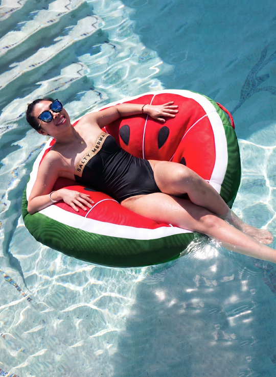Woman relaxing on a red and green Big Joe watermelon slice pool float in the water
