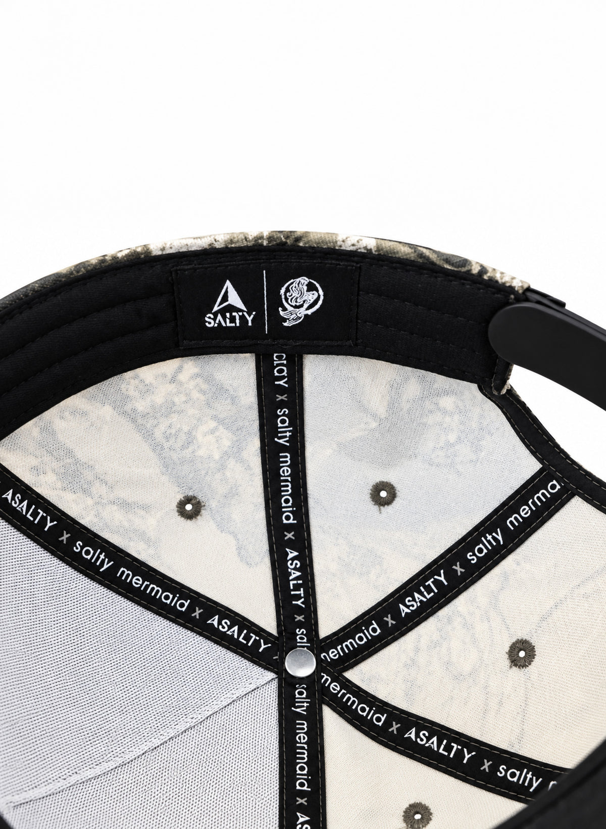 Inside Salty Mermaid camo hat with cream lining, black sweatband and seam tape, white branding and a brown camo edge.

